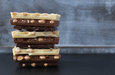 Siyah arka planda fındıklı siyah, beyaz ve sütlü çikolatalar var.