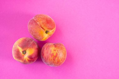 Pembe arka planda üç olgun şeftali, yakın plan.