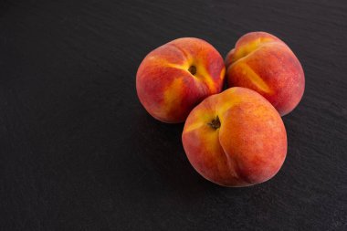 Olgun üç şeftali siyah bir arkaplanda yatıyor, yakın plan.