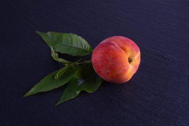 Bir şeftali ve yeşil yapraklar, siyah bir arkaplanda uzan, yakın plan.