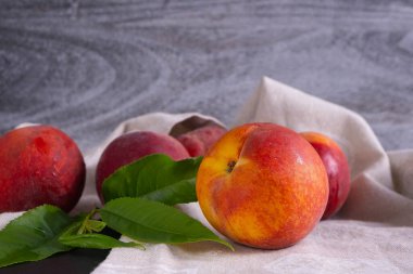 Sulu ve olgun şeftaliler ve yeşil yapraklar bir peçetenin üzerinde uzanır.