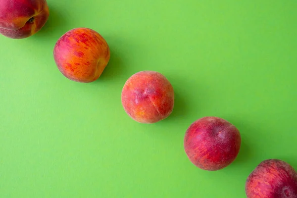 ripe peaches laid out in a line, dividing the green background in half, close-up