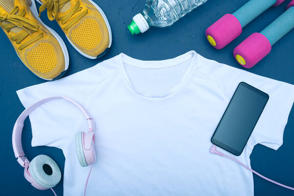 white t-shirt and yellow sneakers, bottle of water and dumbbells, cell phone with headphones, blue background