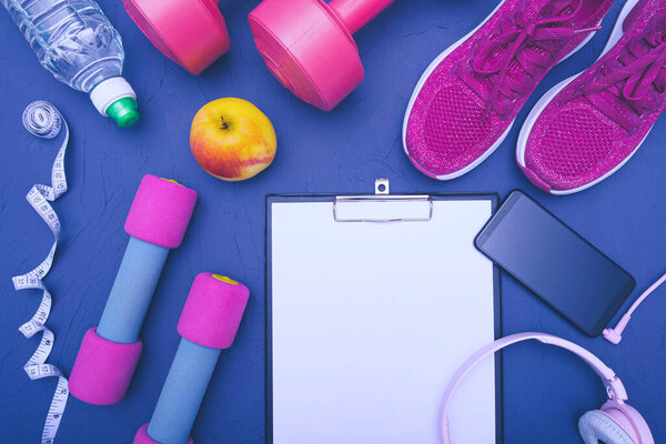 sports equipment - clothes, sneakers, dumbbells apple and a bottle of water, mobile phone with headphones, measuring tape, blue background