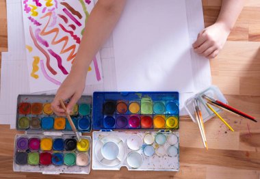 Çocuk renkli boyalarla resim çiziyor, boyaları fırçayla karıştırıyor, yakın plan.