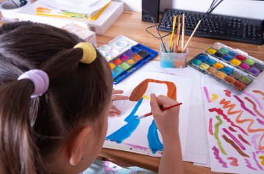 Küçük bir kız renkli boyalarla resim çiziyor. Kağıt üzerinde fırçayla kurşun çekiyor. Yakın plan.