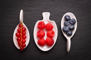 olgun böğürtlen - ahududu, kırmızı frenk üzümü ve yaban mersini, siyah arkaplanda beyaz bir tabakta yatar.