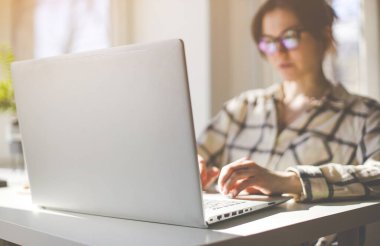 Ofisteki kadın masada oturuyor ve bir dizüstü bilgisayar üzerinde çalışıyor.