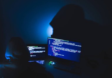 Kapüşonlu bilgisayar korsanı silueti, laptop kullanan ve veri çalmak için monitör kullanan adam. Sanal suç kavramı.