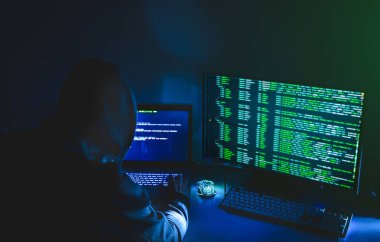Kapüşonlu bilgisayar korsanı silueti, laptop kullanan ve veri çalmak için monitör kullanan adam. Sanal suç kavramı.