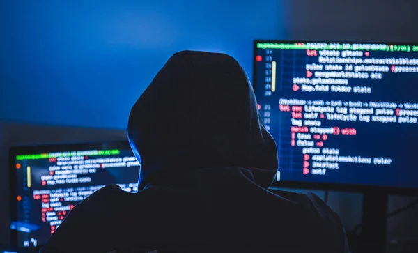 Kapüşonlu bilgisayar korsanı silueti, laptop kullanan ve veri çalmak için monitör kullanan adam. Sanal suç kavramı.