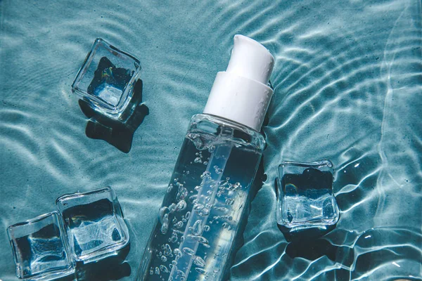 Glas Serum auf einem Hintergrund aus blauem Wasser mit Eis. Hautpflegekonzept — Stockfoto