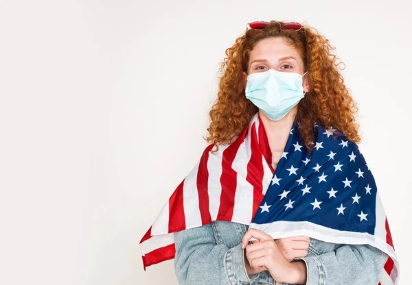 Szczęśliwa piękna młoda kobieta w masce medycznej trzymać flagę, odizolowany na białym tle. Patriotyczny święto i święto niezależność dzień USA 4 lipiec. koronawirusy kwarantanny covid-19 — Zdjęcie stockowe