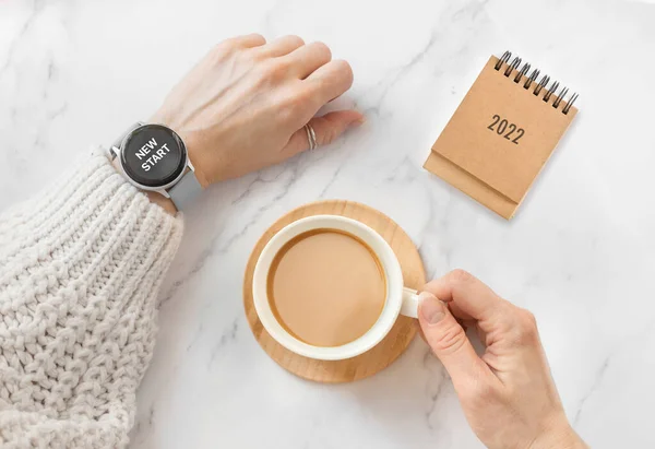 woman hands with watch and cup coffee on table, calendar 2022. Goals and plan for new year