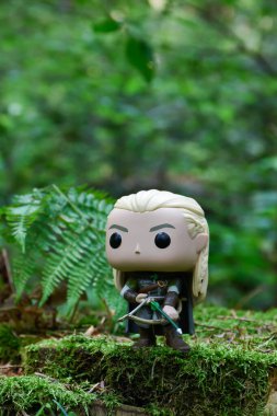 Fantezi filmi Yüzüklerin Efendisi 'ndeki Elf Legolas' ın aksiyon figürü. Ok ve yay tutan savaşçı. Yeşil orman, yosun, eğreltiotu yaprakları.
