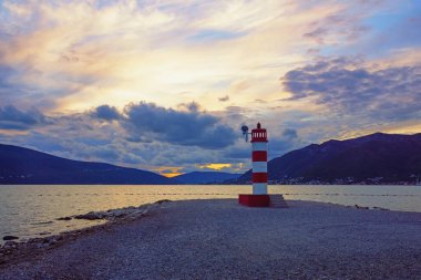 Sonbahar günbatımı, akşam Akdeniz manzarası. Tivat şehri yakınlarındaki Kotor Körfezi kıyısında kırmızı ve beyaz çizgili fener. Karadağ