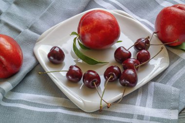 Kırmızı meyveler. Beyaz tabakta taze kirazlar ve nektarinler.