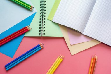 Okul ve hobi kavramları. Renkli kâğıt çarşaflar, renkli kalemler ve pembe kağıt üzerine not defterleri. Boşluğu kopyala