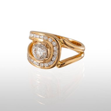 Merkezi elmaslı ve parlak kesilmiş elmaslardan oluşan 18 kt 'lık sarı bir yüzük. Yansımalı beyaz bir arkaplanda fotoğraflandı.