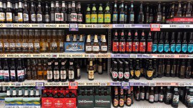 Çeşitli markalardan bira şişeleri süpermarket raflarında sıraya dizildi. Ulusal ve uluslararası bira seçimi. Udine, İtalya. 7 Ocak 2026