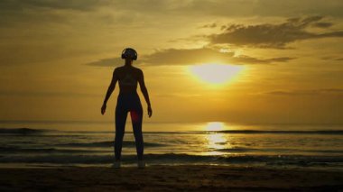 Gün batımında sahilde yoga yaparken genç bir kadın silüeti