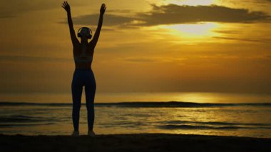 Gün doğumunda sahilde egzersiz yapan bir kadın, siluet.