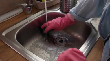 Kadın mutfak lavabosunu deterjanla temizliyor.