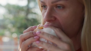 Genç bir kadın kafede sandviç yiyor..