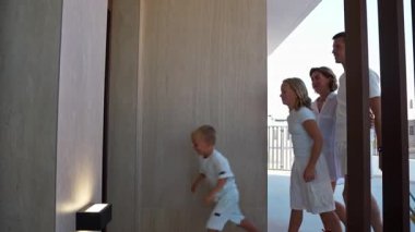 Beyaz tişörtlü ve siyah elbiseli bir adam otelin koridorunda yürüyor..