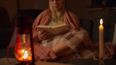 Evde rahat bir kanepede oturmuş kitap okuyan genç bir kadın..