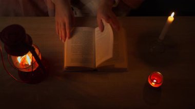 Elinde kitap, elinde mum olan beyaz elbiseli bir kadın karanlık odada.