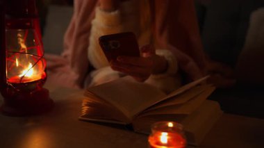 Genç bir kadın mumla kitap okuyor.