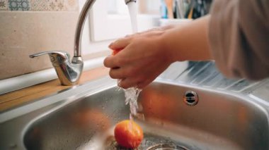Kadın taze portakalları paslanmaz çelik bir lavaboda yıkayarak hazırlıyor. Bir portakalı akan suyun altında tutarken, bir kaç tanesi de lavaboya ve yakınlardaki bir kaseye yerleştiriliyor.