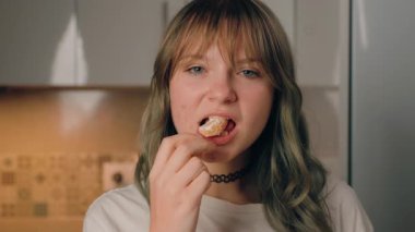 Uzun sarı saçlı bir kadın, açık havada durur, kitap okur ve sayfalarını çevirir, yanında yeşil bir bitki, açık mavi gökyüzüne karşı parlak, güneşli bir ortamda görünür.