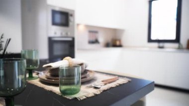 Modern mutfak sahnesi, çağdaş bir ev ortamında parlak ve minimalist bir tasarımı vurgulayan, siyah bir tezgahın üzerinde yeşil bardaklar, tabaklar ve çatal bıçaklarla güzel bir set masası sergiliyor.