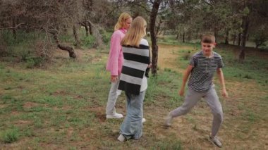 Üç genç kadın ve bir çocuk yeşil bir parkta, pembe kazak giyen bir kadın, çizgili bir bluz giyen bir erkek ve arka planda onlara doğru koşan bir çocuk.