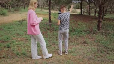 Pembe kazaklı bir kadın çizgili tişörtlü bir oğlanla ilişkiye girmek için eğilirken başka bir çocuk yemyeşil bir ormanda çevreyi araştırıyor ve bir etkileşim ve keşif anını vurguluyor.