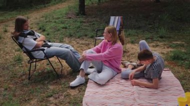 Genç yetişkinler, sakin bir ortamda ağaçların ve çimenlerin arka planına kurulmuş, bir kadının oturduğu ve diğer ikisinin etkileşim halinde olduğu bir battaniyenin üzerinde gelişigüzel bir şekilde toplanmaktan hoşlanırlar.