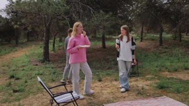 Genç arkadaşlar yeşil bir parkta piknik yapmak için toplanırken, bir kız bir tabak yemek tutarken, diğer ikisi yakınlarda, ağaçlar ve çimenlerin üzerinde piknik battaniyeleri ile sohbet ediyorlar.