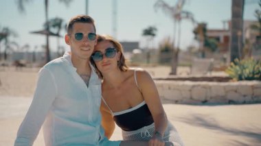 Mutlu bir çift genç adam ve kadın güneş gözlüğü takıyor ve yazın plajda şık kıyafetler giyiyor.