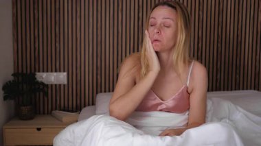 Beyaz cüppeli genç kız yatağa oturur ve kameraya bakar. Sabah yatak odasında..