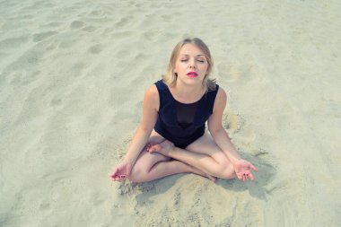 Top view of a young woman kneeling with her eyes closed in a black swimsuit