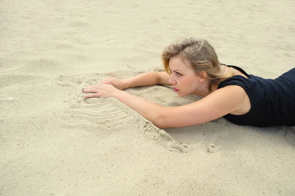 Young woman in a black swimsuit is lying on the sand in the desert