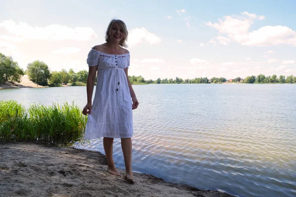Young woman in a white dress walks near a lake in nature