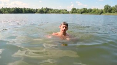 Genç, çıplak, sportif adam gölün üstünde suyun altından çıkıyor. Yüzme, dinlenme, spor