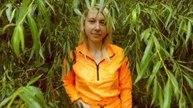 Yeşil yapraklı, turuncu elbiseli genç sarışın kadın.