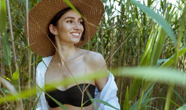 Şapkalı genç bir kadın ormanda gülümsüyor. Uzun sazlıklar doğada