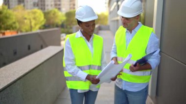 Erkek İnşaat Alanı Yöneticisi Afrika kökenli Amerikalı kadın mimarla açık havada plan hakkında konuşuyor.