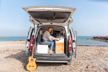 Gitarlı bir kadın, plajda karavan hayatından hoşlanıyor.