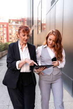 Anne iş kadını ve yetişkin kız dışarıda dijital tablet kullanarak yürürken iş birliği yapıyorlar.
